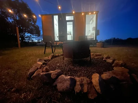 Tiny home glowing at night beyond a stone firepit.